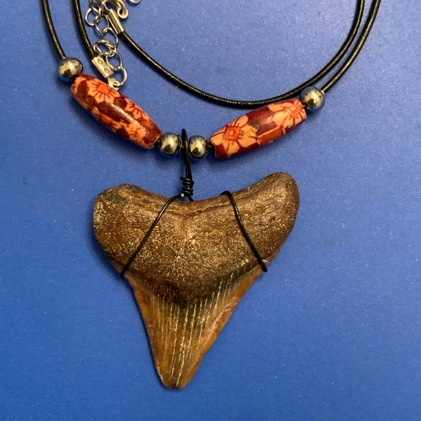 Real shark tooth necklace made from a fossil megalodon shark tooth pendant wrapped with black wire, hung on a black cotton cord with colorful beads