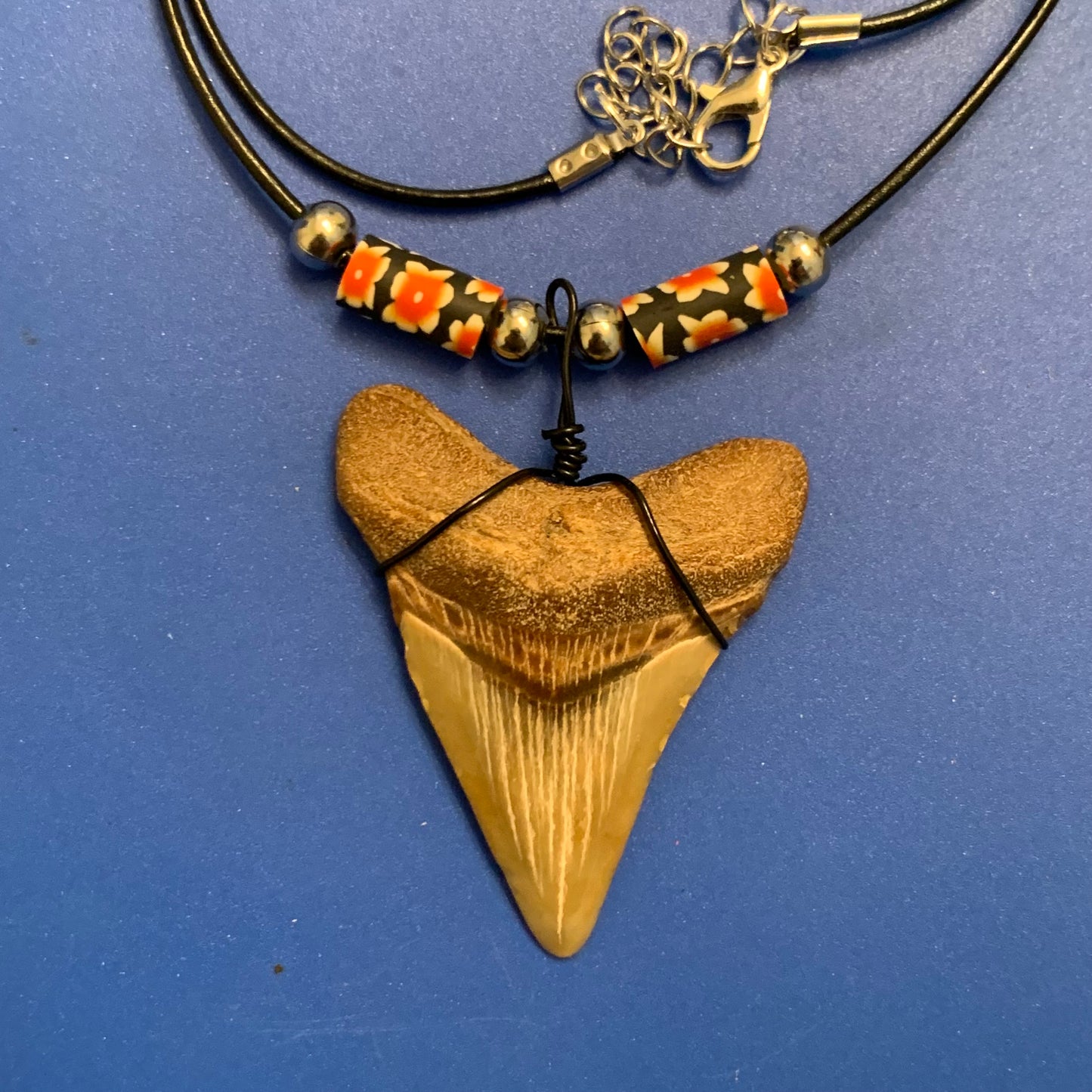 Real shark tooth necklace made from a fossil megalodon shark tooth pendant wrapped with black wire, hung on a black cotton cord with colorful beads