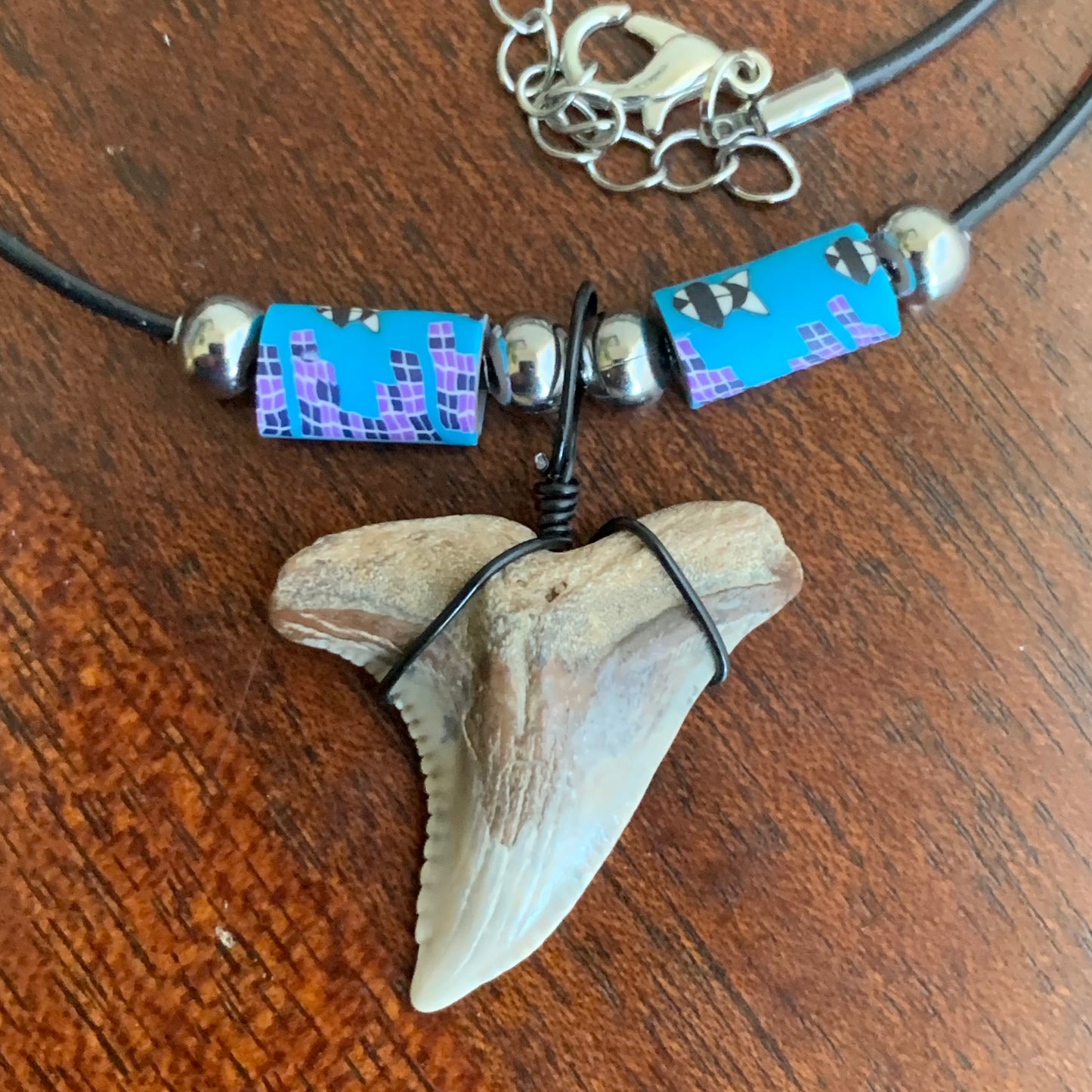 Real shark tooth necklace made from a fossil snaggle shark tooth pendant wrapped with black wire, hung on a black cotton cord with colorful beads