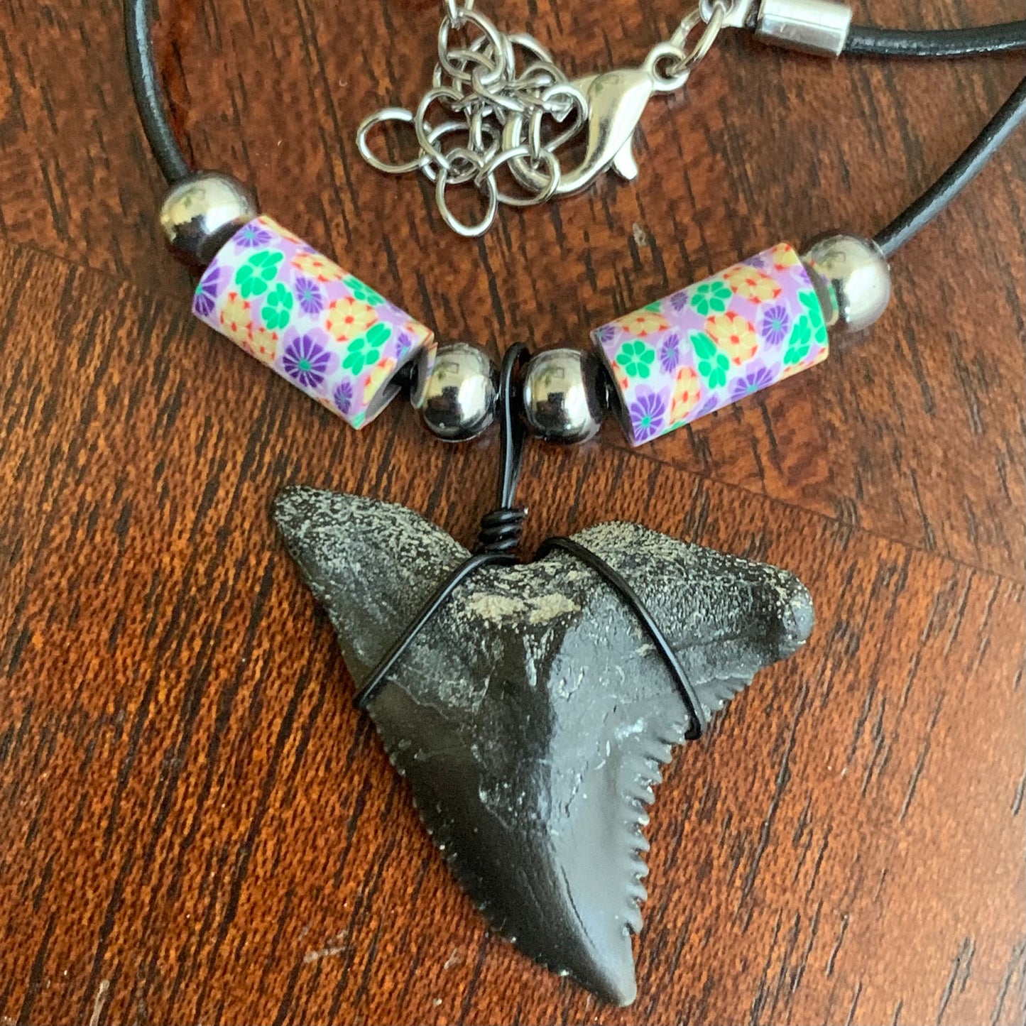 Real shark tooth necklace made from a fossil snaggle shark tooth pendant wrapped with black wire, hung on a black cotton cord with colorful beads