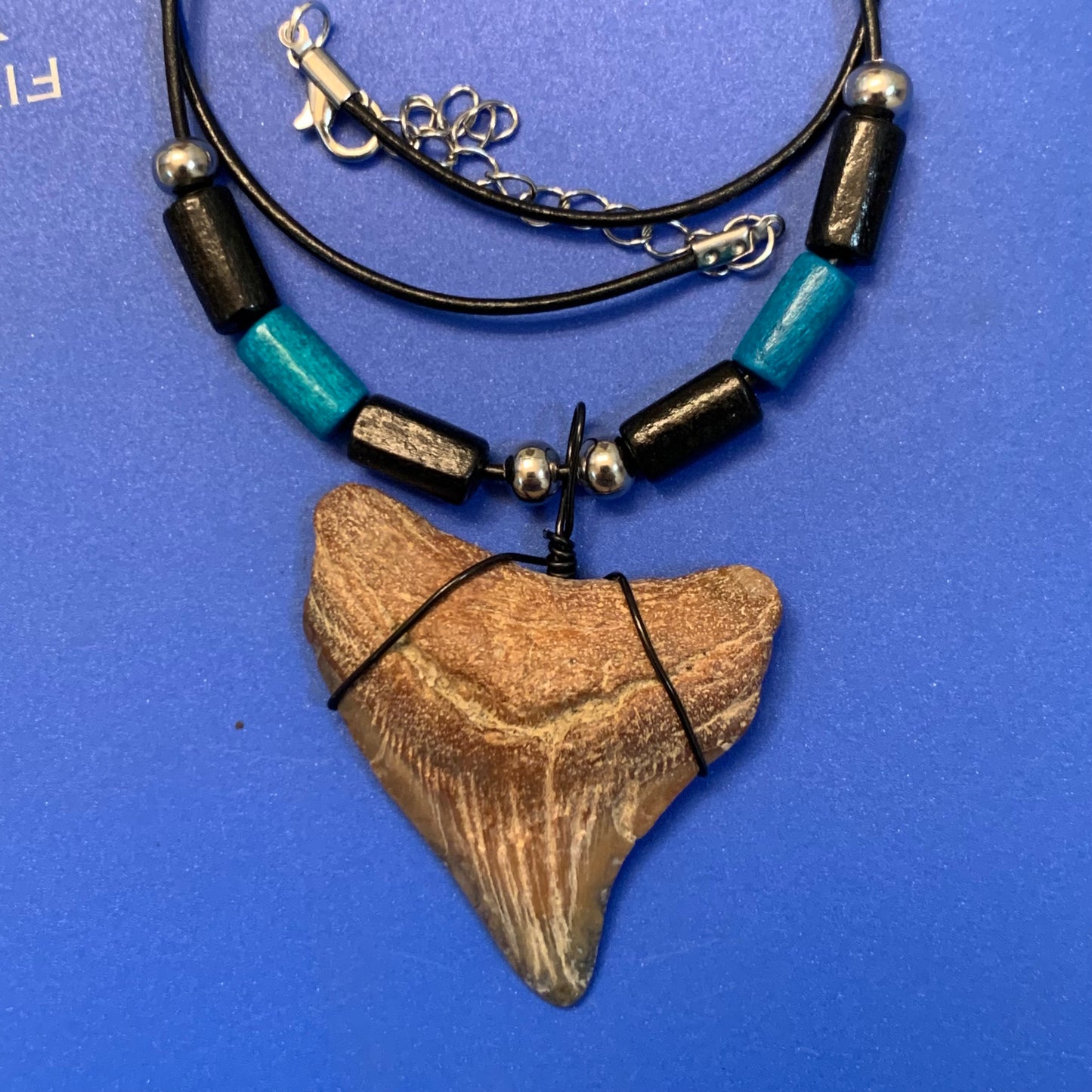 Real shark tooth necklace made from a fossil megalodon shark tooth pendant wrapped with black wire, hung on a black cotton cord with colorful beads
