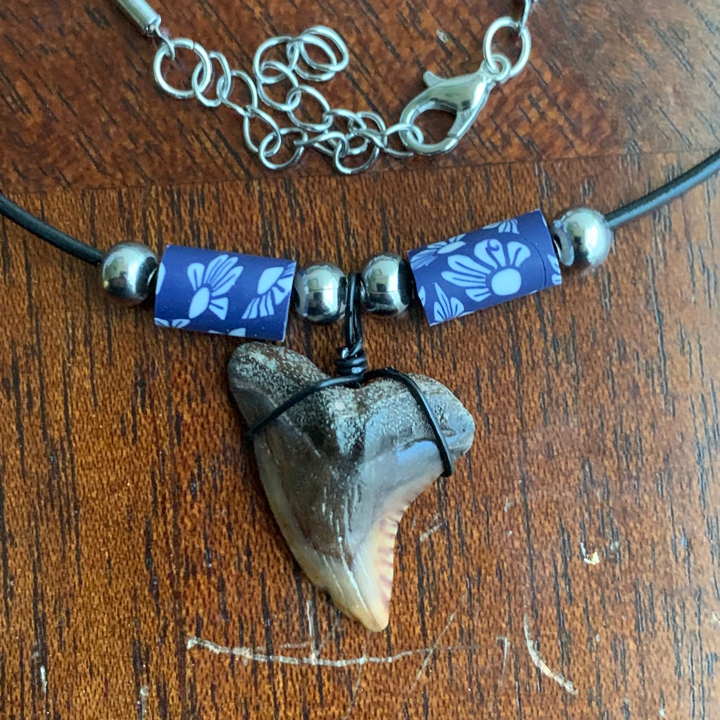 Real shark tooth necklace made from a fossil snaggle shark tooth pendant wrapped with black wire, hung on a black cotton cord with colorful beads
