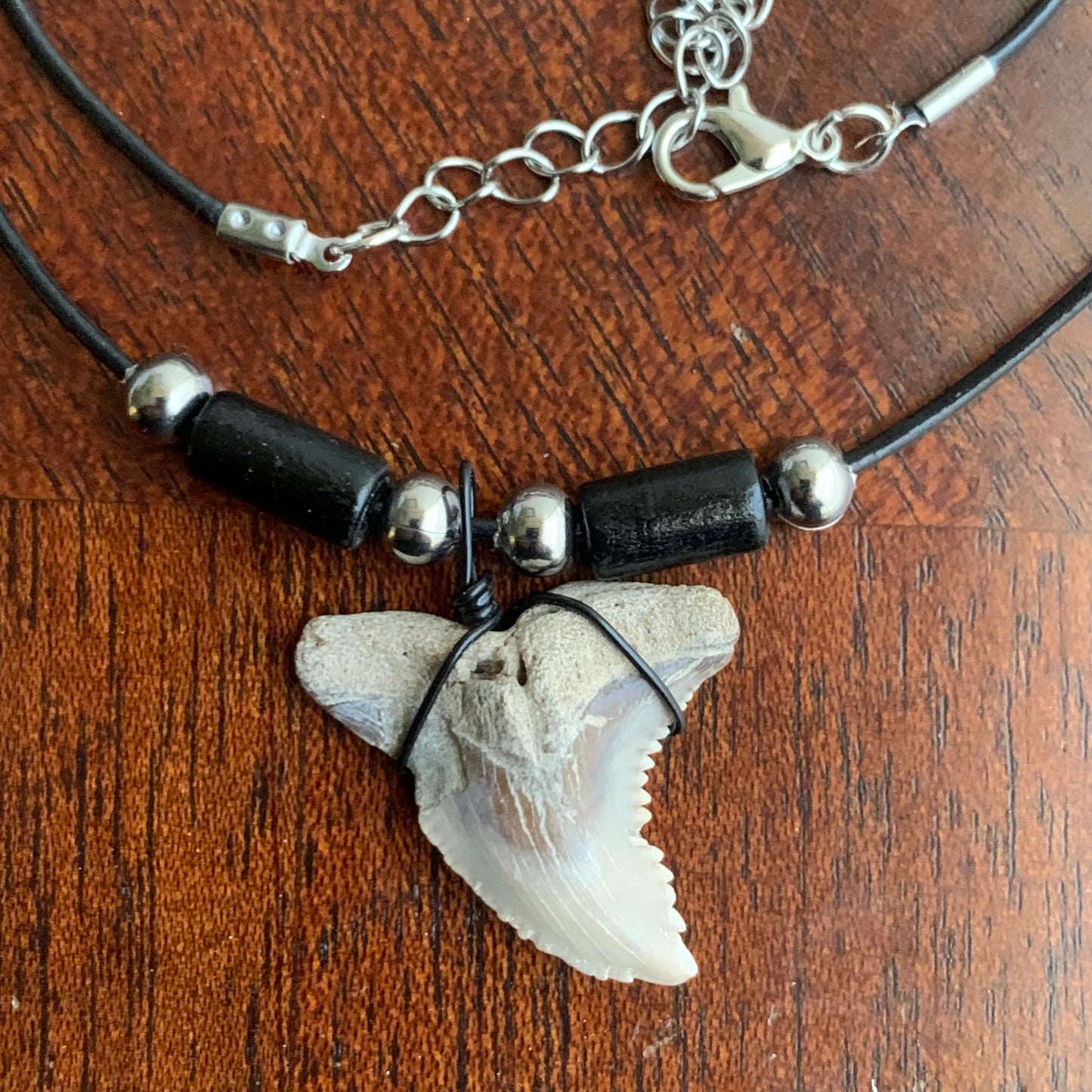 Real shark tooth necklace made from a fossil snaggle shark tooth pendant wrapped with black wire, hung on a black cotton cord with colorful beads