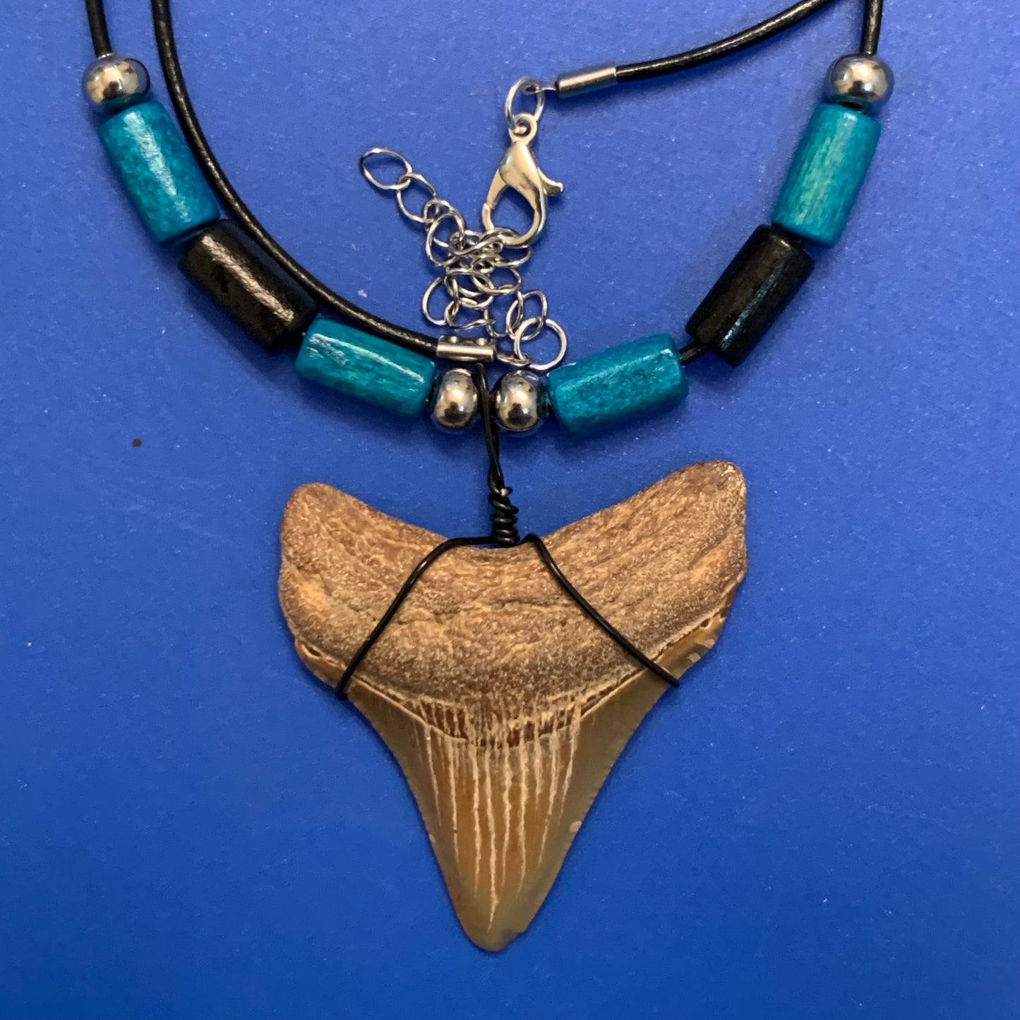 Real shark tooth necklace made from a fossil megalodon shark tooth pendant wrapped with black wire, hung on a black cotton cord with colorful beads