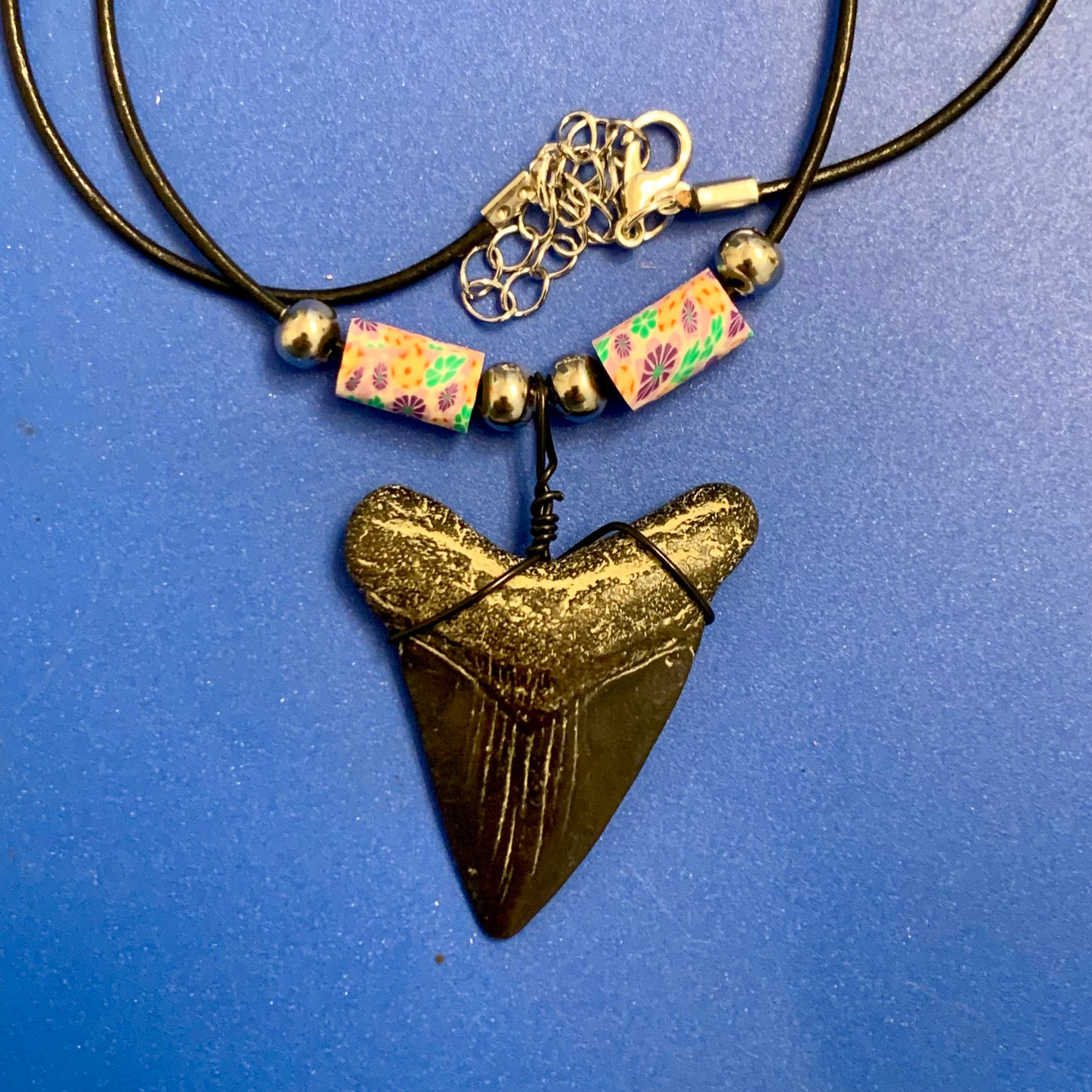 Real shark tooth necklace made from a fossil megalodon shark tooth pendant wrapped with black wire, hung on a black cotton cord with colorful beads