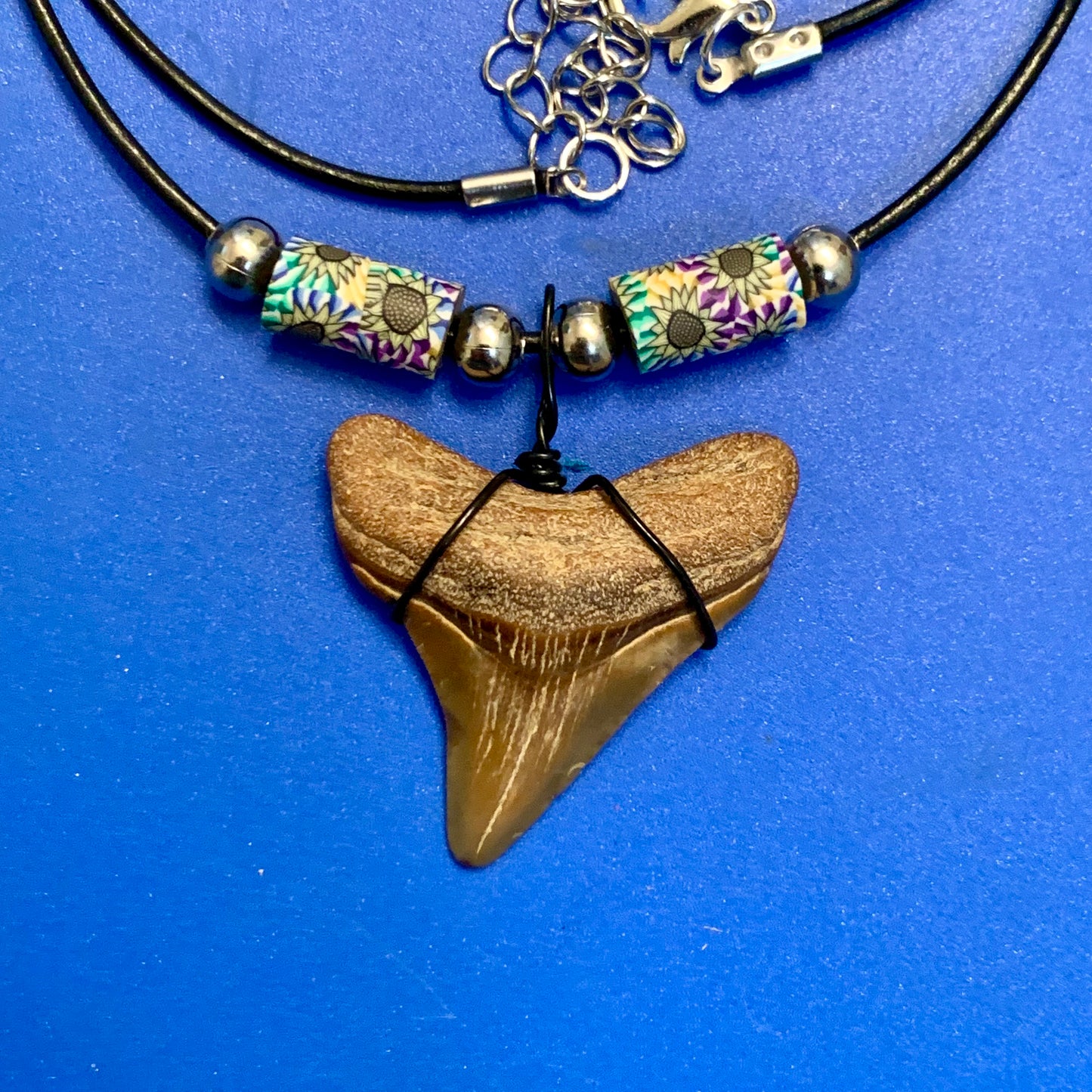 Real shark tooth necklace made from a fossil megalodon shark tooth pendant wrapped with black wire, hung on a black cotton cord with colorful beads