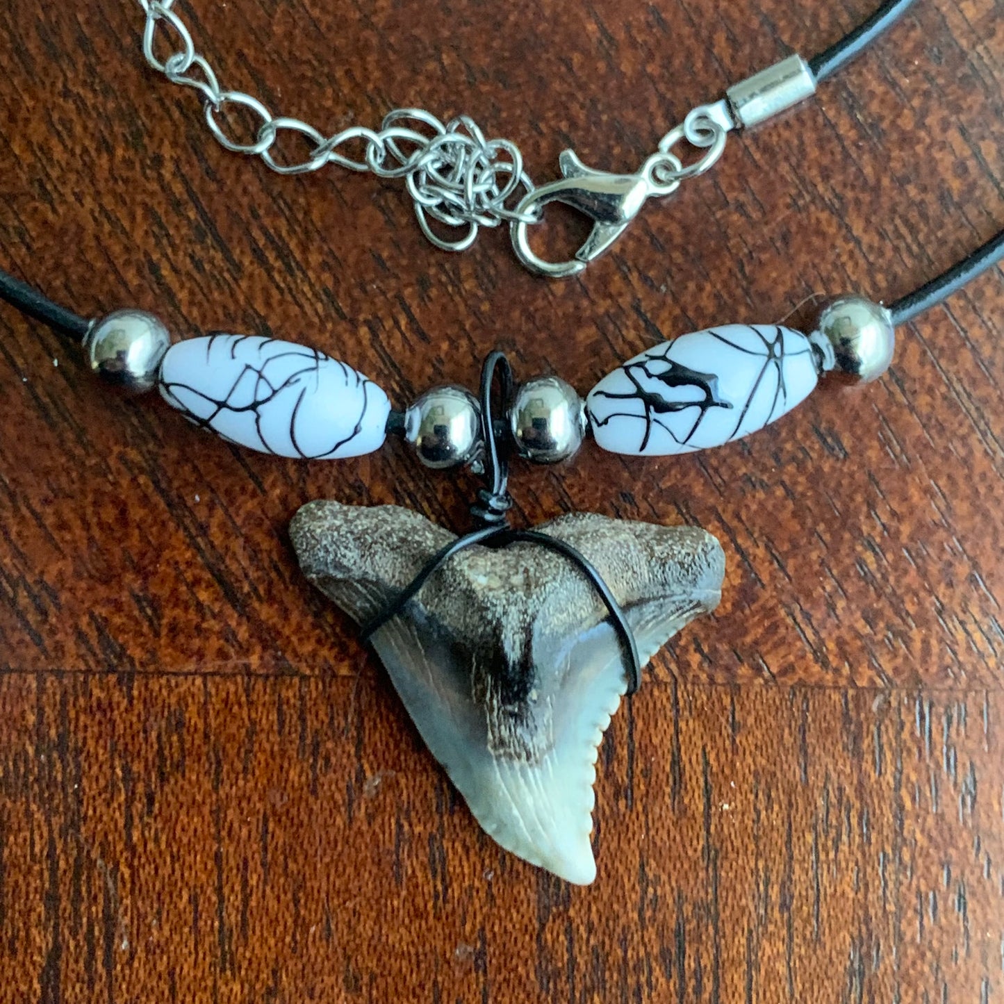 Real shark tooth necklace made from a fossil snaggle shark tooth pendant wrapped with black wire, hung on a black cotton cord with colorful beads