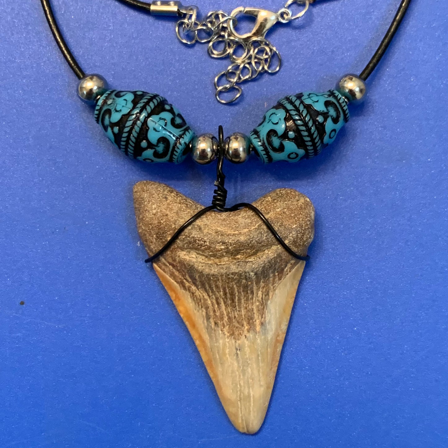 Real shark tooth necklace made from a fossil megalodon shark tooth pendant wrapped with black wire, hung on a black cotton cord with colorful beads