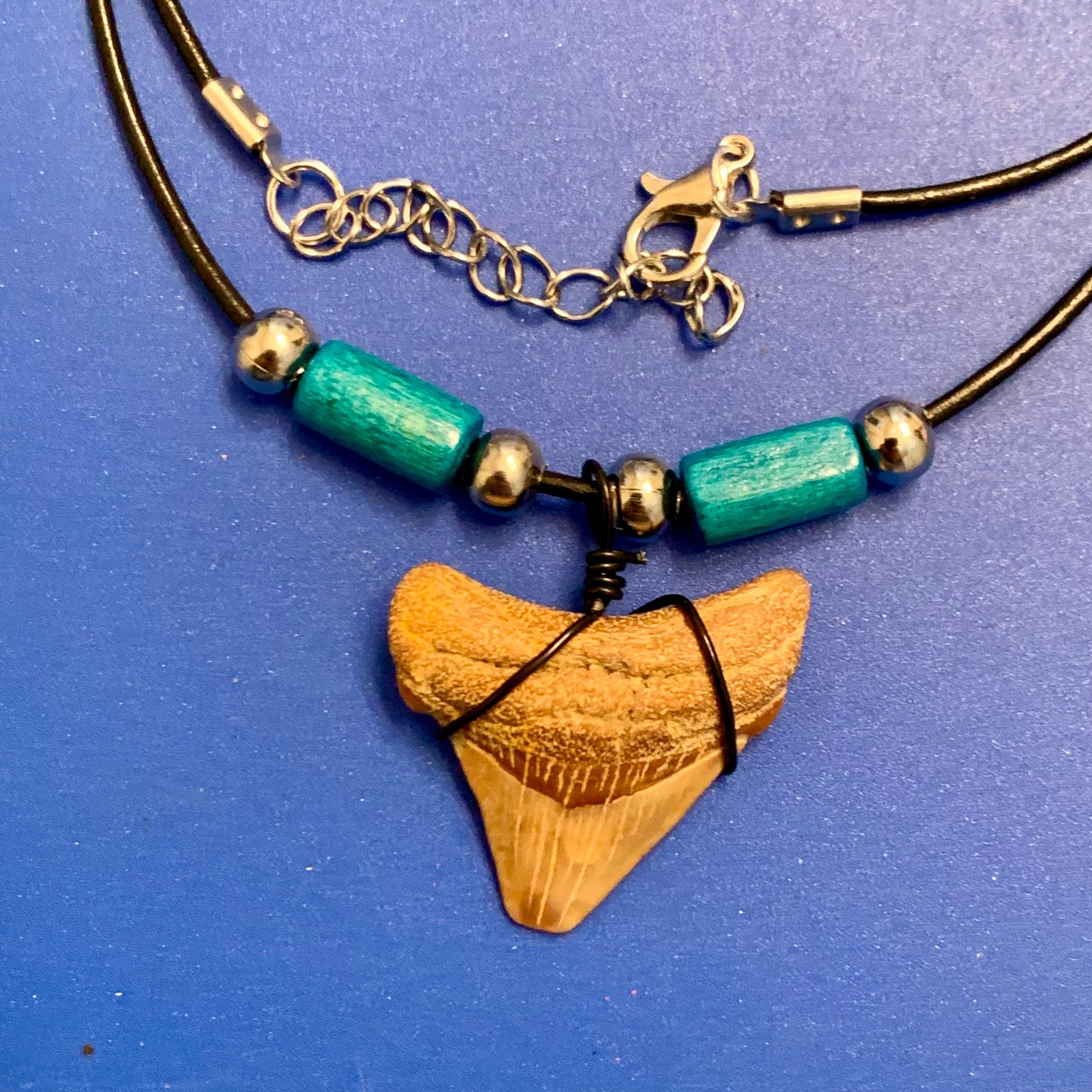 Real shark tooth necklace made from a fossil megalodon shark tooth pendant wrapped with black wire, hung on a black cotton cord with colorful beads