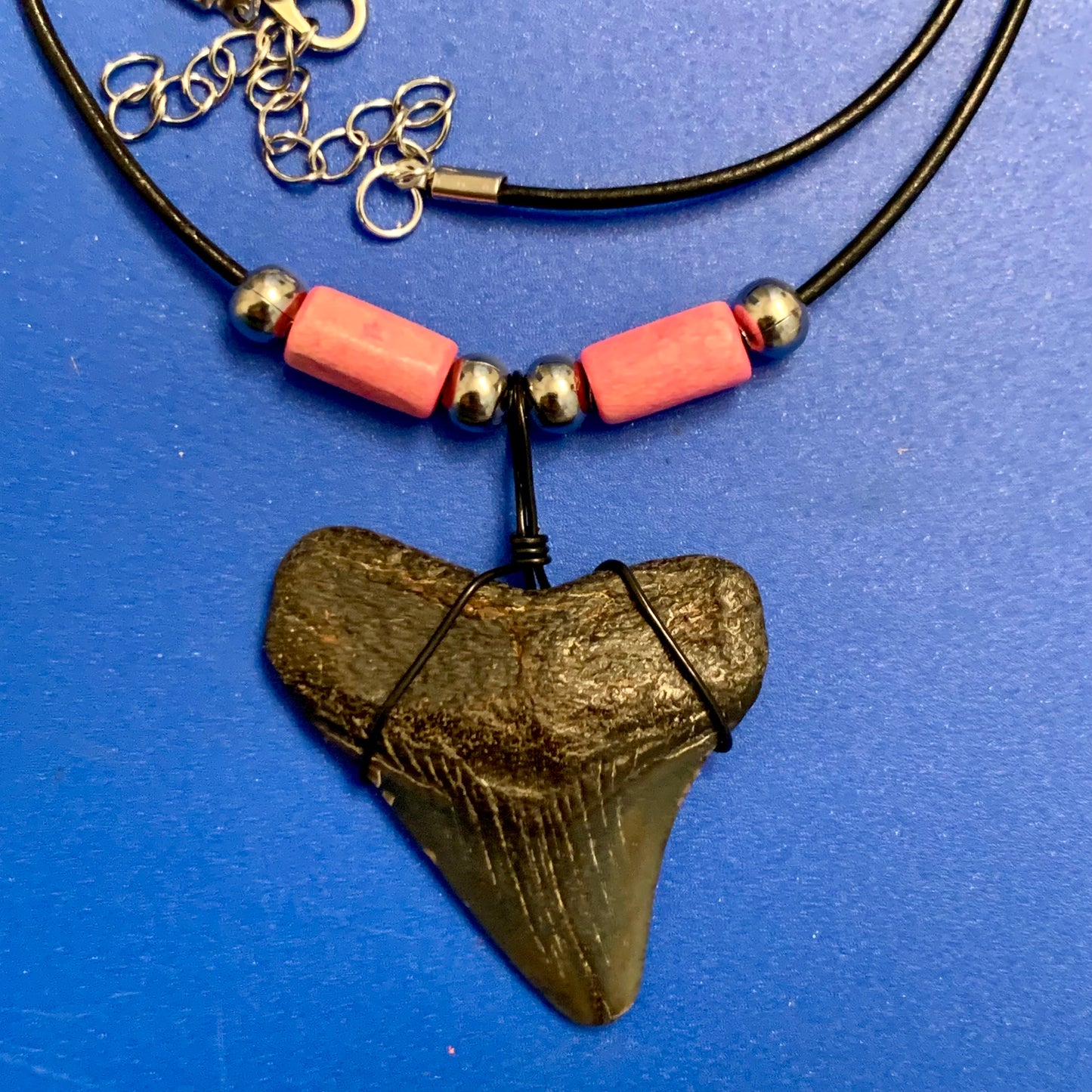 Real shark tooth necklace made from a fossil megalodon shark tooth pendant wrapped with black wire, hung on a black cotton cord with colorful beads