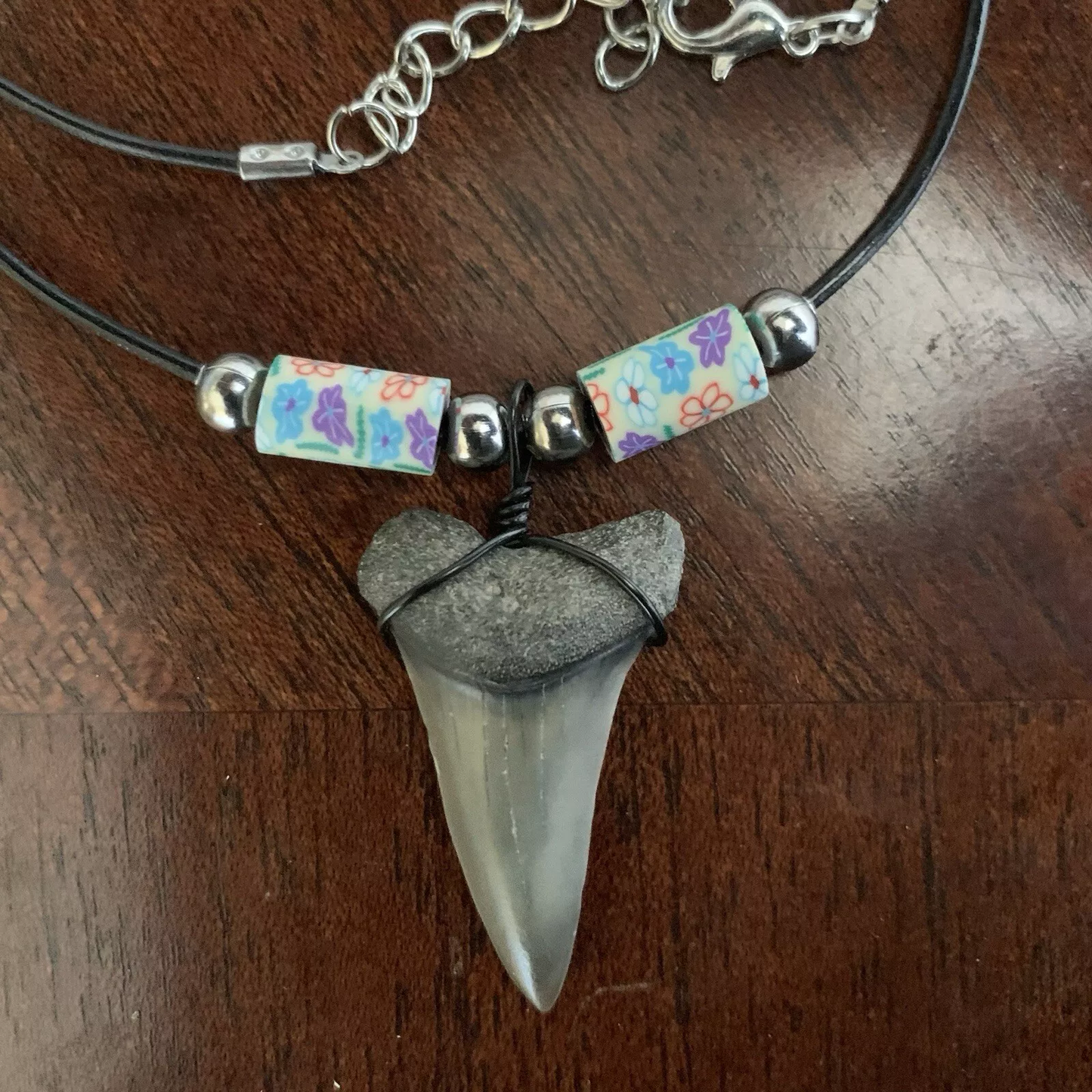 Real shark tooth necklace made from a fossil lesser white shark tooth pendant wrapped with black wire, hung on a black cotton cord with colorful beads