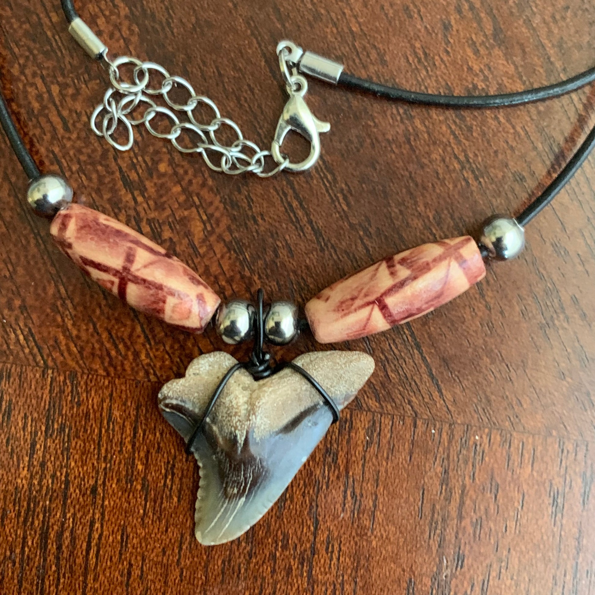 Real shark tooth necklace made from a fossil snaggle shark tooth pendant wrapped with black wire, hung on a black cotton cord with colorful beads