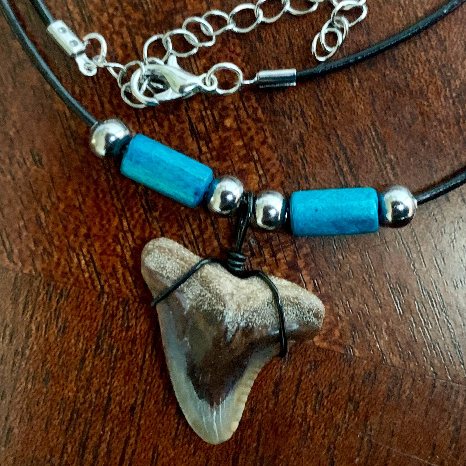 Real shark tooth necklace made from a fossil snaggle shark tooth pendant wrapped with black wire, hung on a black cotton cord with colorful beads