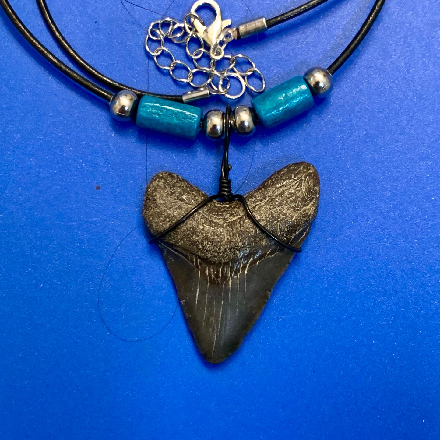 Real shark tooth necklace made from a fossil megalodon shark tooth pendant wrapped with black wire, hung on a black cotton cord with colorful beads