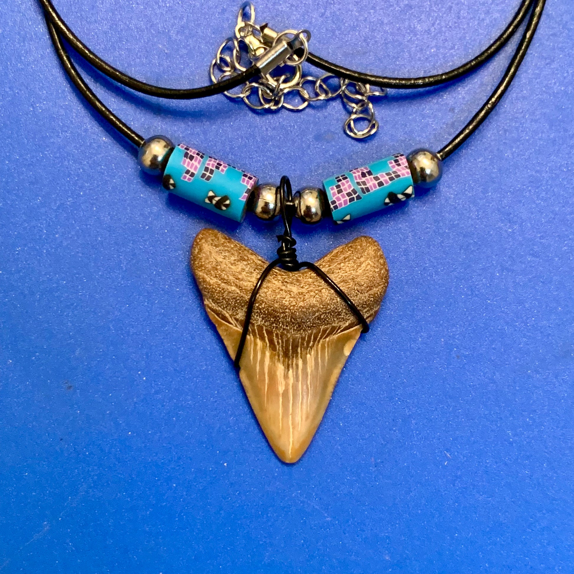 Real shark tooth necklace made from a fossil megalodon shark tooth pendant wrapped with black wire, hung on a black cotton cord with colorful beads