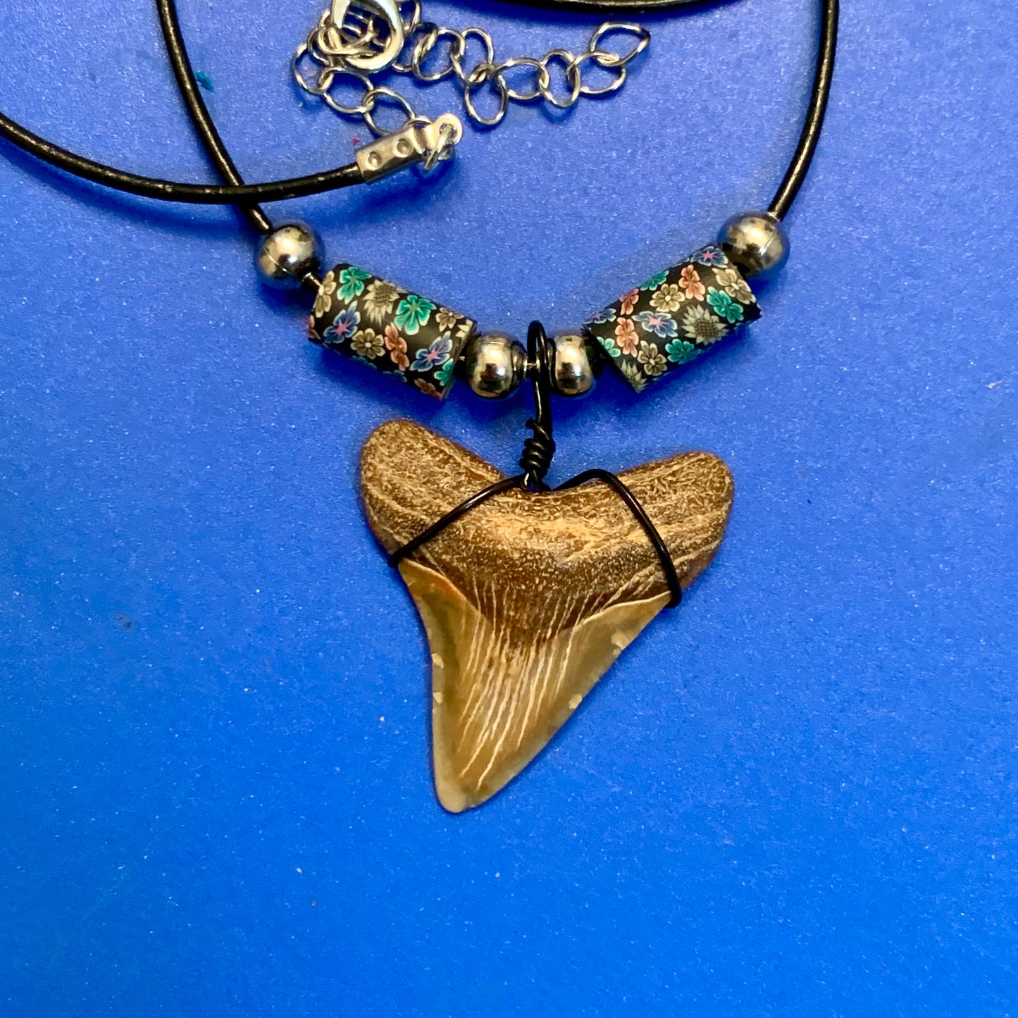 Real shark tooth necklace made from a fossil megalodon shark tooth pendant wrapped with black wire, hung on a black cotton cord with colorful beads