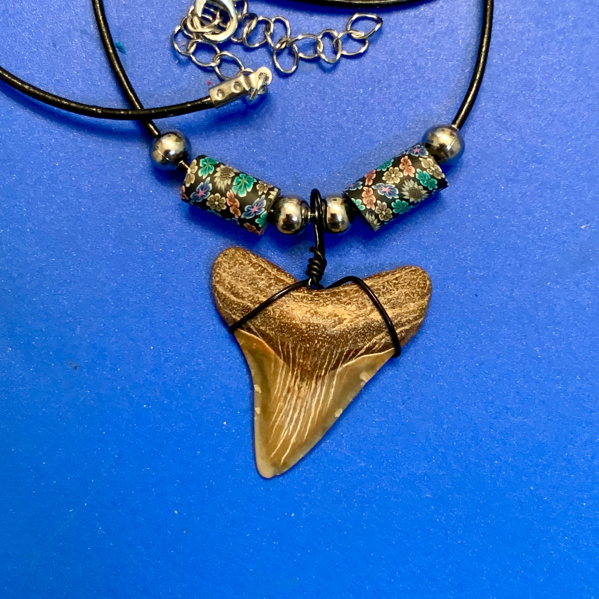 Real shark tooth necklace made from a fossil megalodon shark tooth pendant wrapped with black wire, hung on a black cotton cord with colorful beads