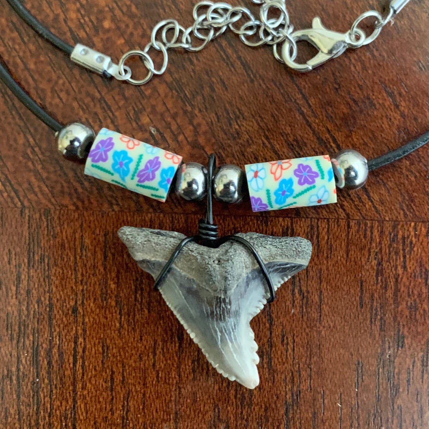 Real shark tooth necklace made from a fossil snaggle shark tooth pendant wrapped with black wire, hung on a black cotton cord with colorful beads