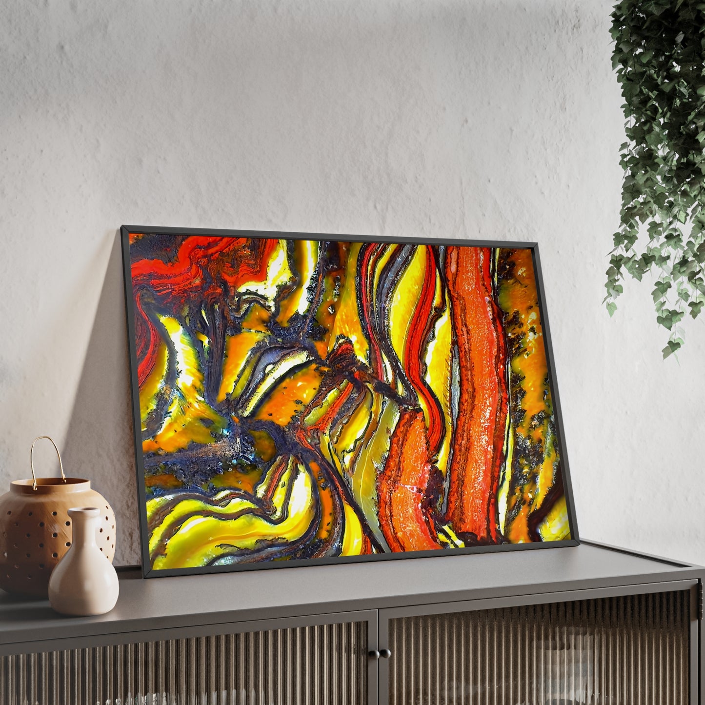 Wall art print capturing a captivating close-up photograph of some faulted and folded tiger iron with its red, yellow and black color. The picture is in a black frame and is leaning against the wall, on a low height cabinet, in the living room.