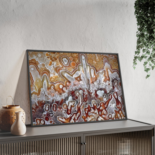 Wall art print capturing a captivating close-up photograph of a lacy agate with its orange, red and white color. The picture is in a black frame and is leaning against the wall, on a low height cabinet, in the living room.
