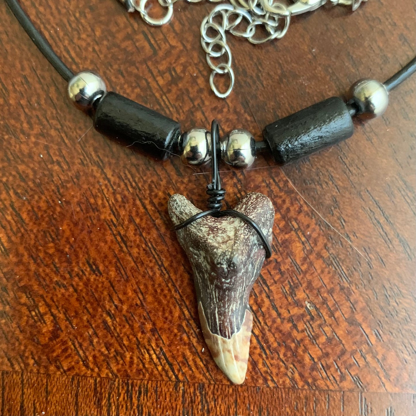 Real shark tooth necklace made from a fossil snaggle shark tooth pendant wrapped with black wire, hung on a black cotton cord with colorful beads