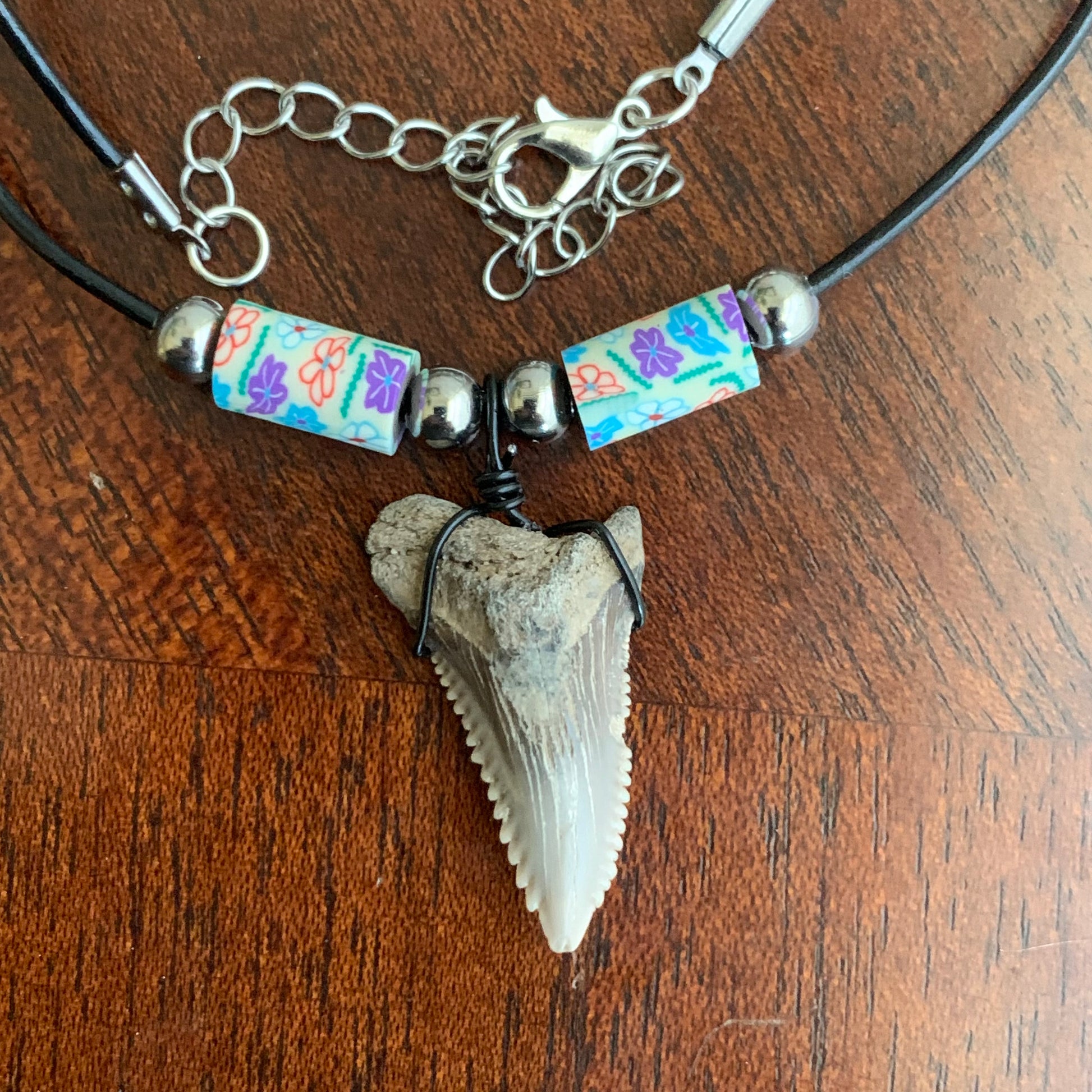 Real shark tooth necklace made from a fossil snaggle shark tooth pendant wrapped with black wire, hung on a black cotton cord with colorful beads