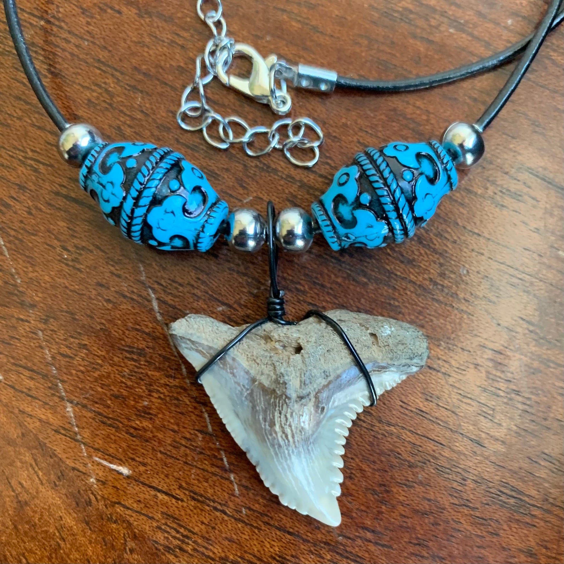Real shark tooth necklace made from a fossil snaggle shark tooth pendant wrapped with black wire, hung on a black cotton cord with colorful beads