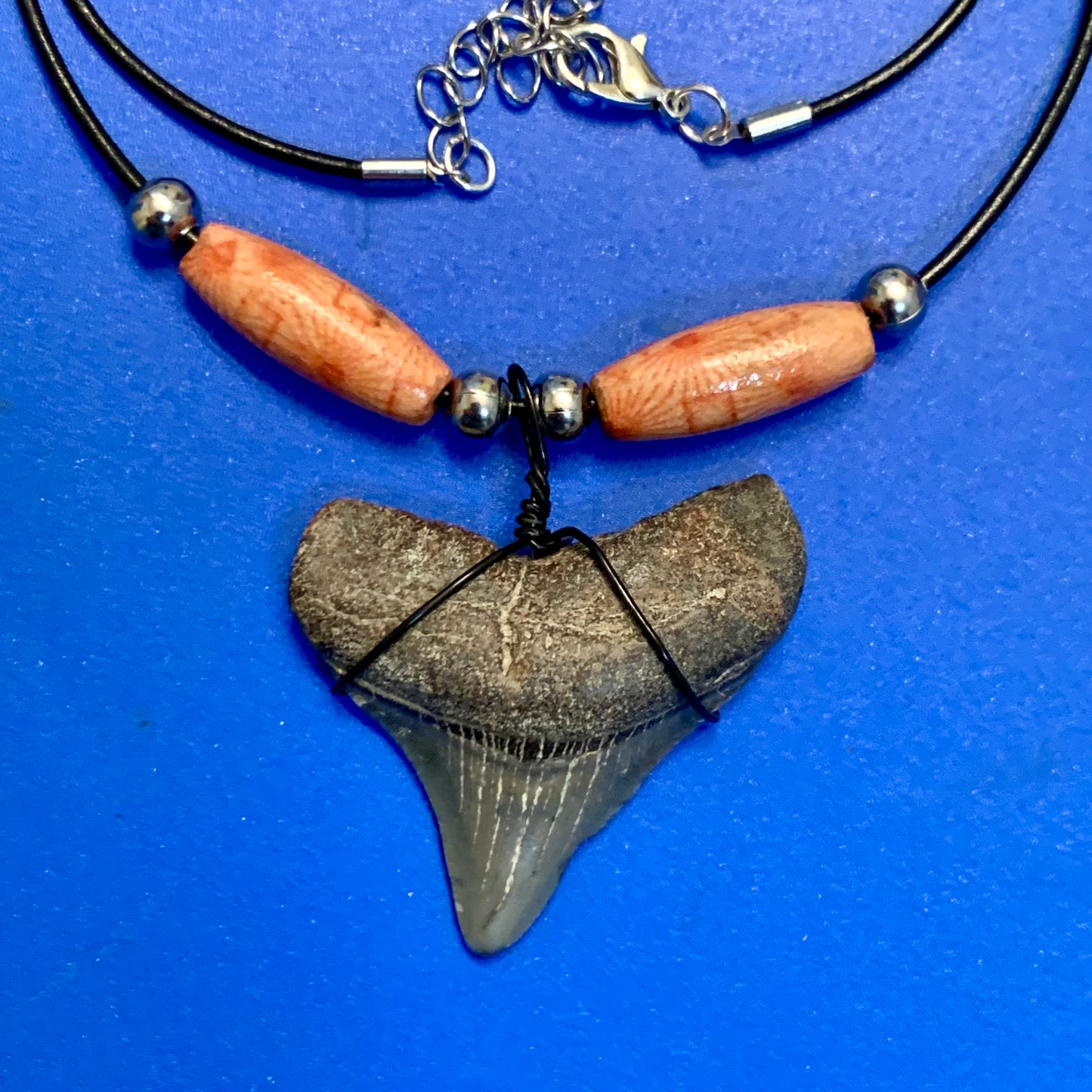 Real shark tooth necklace made from a fossil megalodon shark tooth pendant wrapped with black wire, hung on a black cotton cord with colorful beads