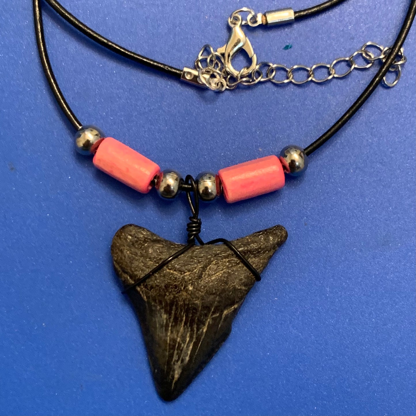 Real shark tooth necklace made from a fossil megalodon shark tooth pendant wrapped with black wire, hung on a black cotton cord with colorful beads